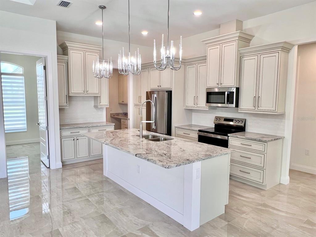 A kitchen features cream-colored cabinets, a granite-topped island with a sink, and stainless steel appliances — 55 ROTONDA CIRCLE, ROTONDA WEST, FL