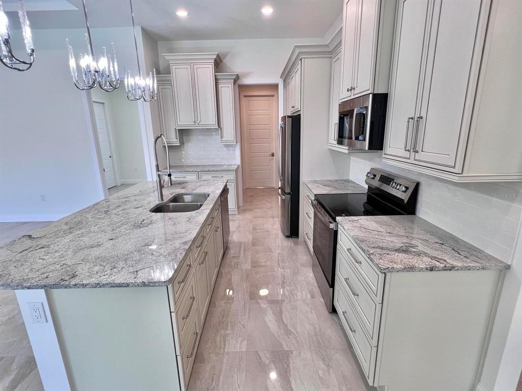 A kitchen features light-colored cabinetry, granite countertops, a center island, and stainless steel appliances — 55 ROTONDA CIRCLE, ROTONDA WEST, FL