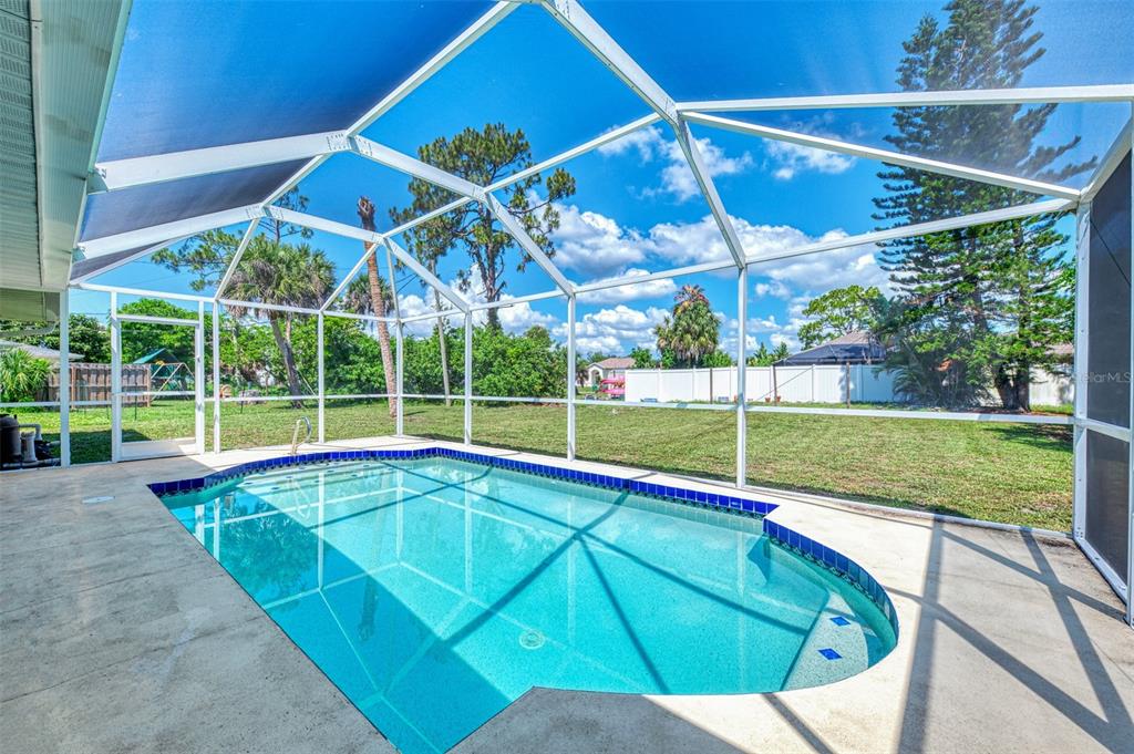 A swimming pool enclosed by a screened lanai overlooks a grassy backyard with trees — 61 SHADE STREET, PORT CHARLOTTE, FL