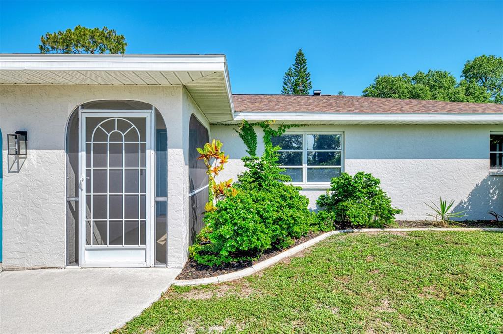 A white stucco house exterior features a screened front door and a large landscape bush — 61 SHADE STREET, PORT CHARLOTTE, FL