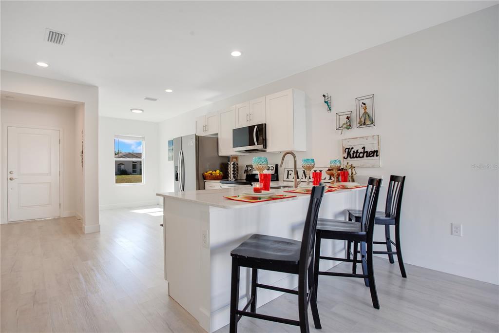 A white kitchen features a center island with bar seating and light-colored wood flooring — 10450 PENDLETON AVENUE UNIT 10452, ENGLEWOOD, FL