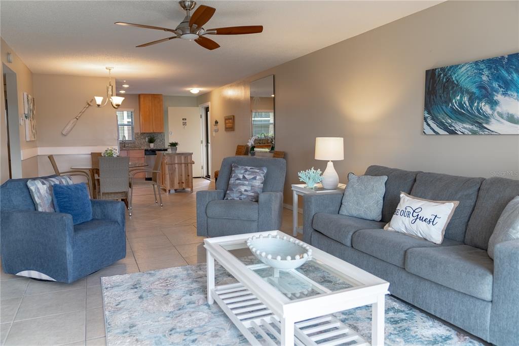 A living room with a gray sofa, blue armchair, and an open kitchen in the background — 925 BEACH ROAD UNIT 107, SARASOTA, FL