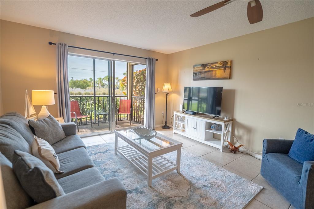 A living room features a gray sofa, blue armchair, white coffee table, and sliding glass doors — 925 BEACH ROAD UNIT 107, SARASOTA, FL