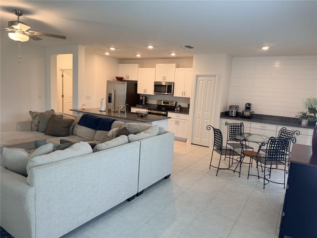 An open-concept kitchen with white cabinets and granite countertops overlooks a living room area — 36434 GARDEN WALL WAY, ZEPHYRHILLS, FL