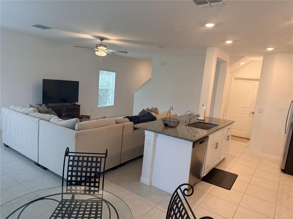 A living room with a sectional sofa and television connects to a kitchen with an island — 36434 GARDEN WALL WAY, ZEPHYRHILLS, FL