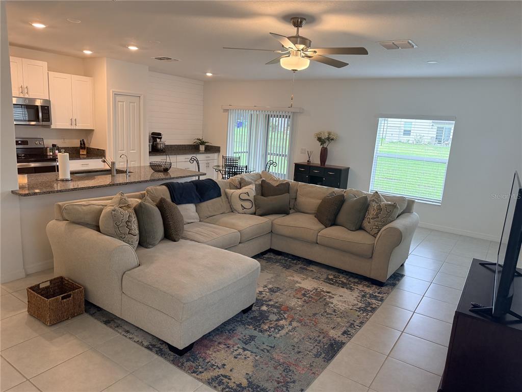 A living room with a large sectional sofa, area rug, and an open-concept kitchen — 36434 GARDEN WALL WAY, ZEPHYRHILLS, FL