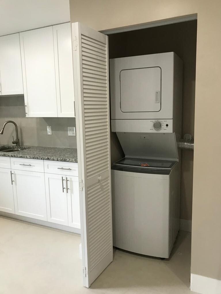 A white stacked washer and dryer unit sits inside a closet next to a kitchen — 17024 89th Place N Apt A, FL 33470, FL