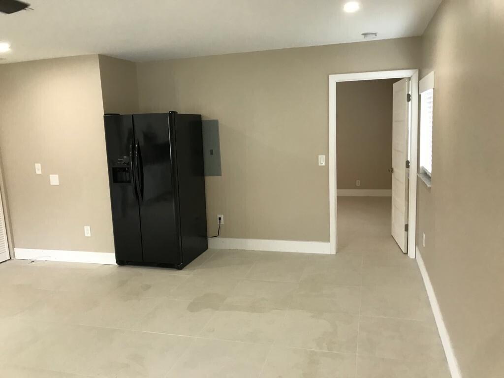 A room with light tile flooring, beige walls, a black refrigerator, and an open doorway — 17024 89th Place N Apt A, FL 33470, FL