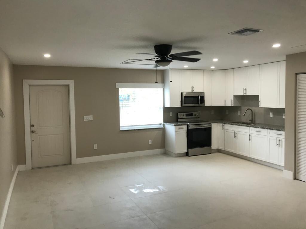 A kitchen with white cabinets and stainless steel appliances opens into a neutral-toned living area — 17024 89th Place N Apt A, FL 33470, FL