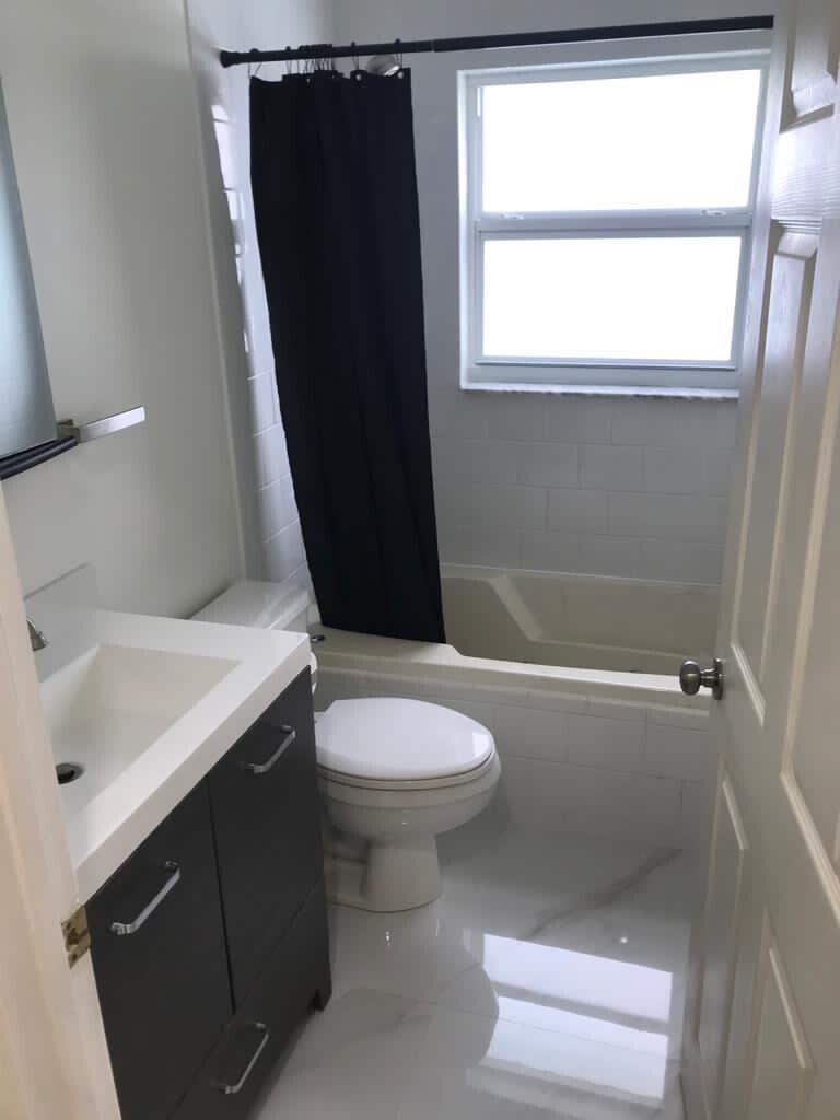 A small bathroom features a dark vanity, white toilet, and a bathtub with a black curtain — 17024 89th Place N Apt A, FL 33470, FL