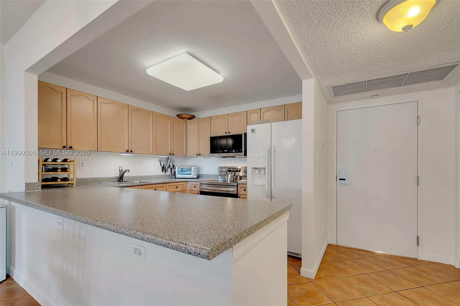 A kitchen features light wood cabinets, granite countertops, and white appliances — 2301 Collins Ave # 533, Miami Beach FL 33139, MIAMI BEACH, FL