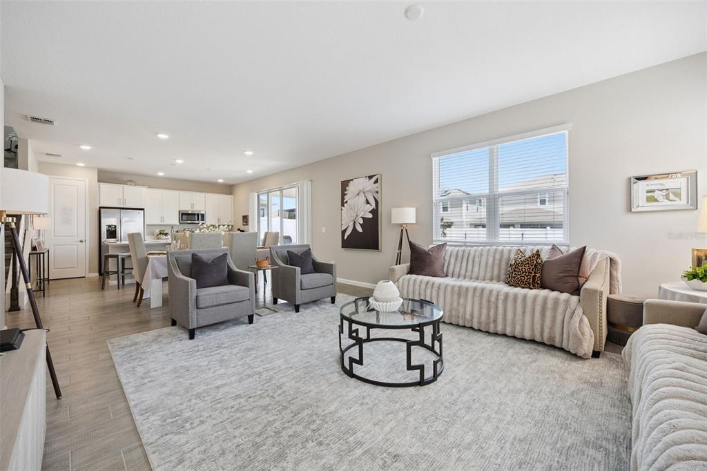 A bright, open-concept living room features a textured sofa, two gray armchairs, and tile flooring — 1550 SUGARBELLE CIRCLE, MASCOTTE, FL
