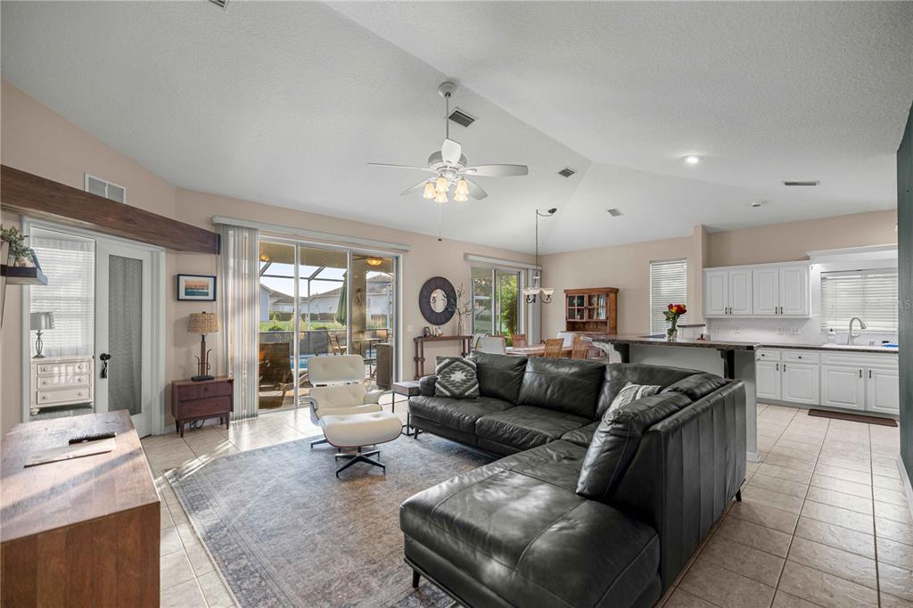 An open-concept living room features a dark leather sectional, white lounge chair, and kitchen area — 2197 NW 55TH AVENUE ROAD, OCALA, FL