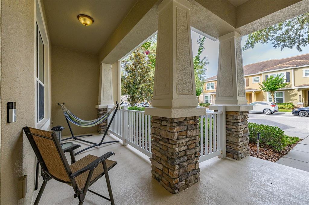 A covered front porch features stone-based pillars, a white railing, a hammock, and a chair — 7435 RIPPLEPOINTE WAY, WINDERMERE, FL