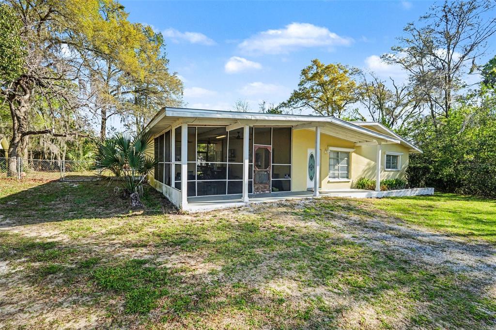 A yellow single-story house features a large screened-in porch and a gravel yard — 9101 S SUNSET POINT, FLORAL CITY, FL