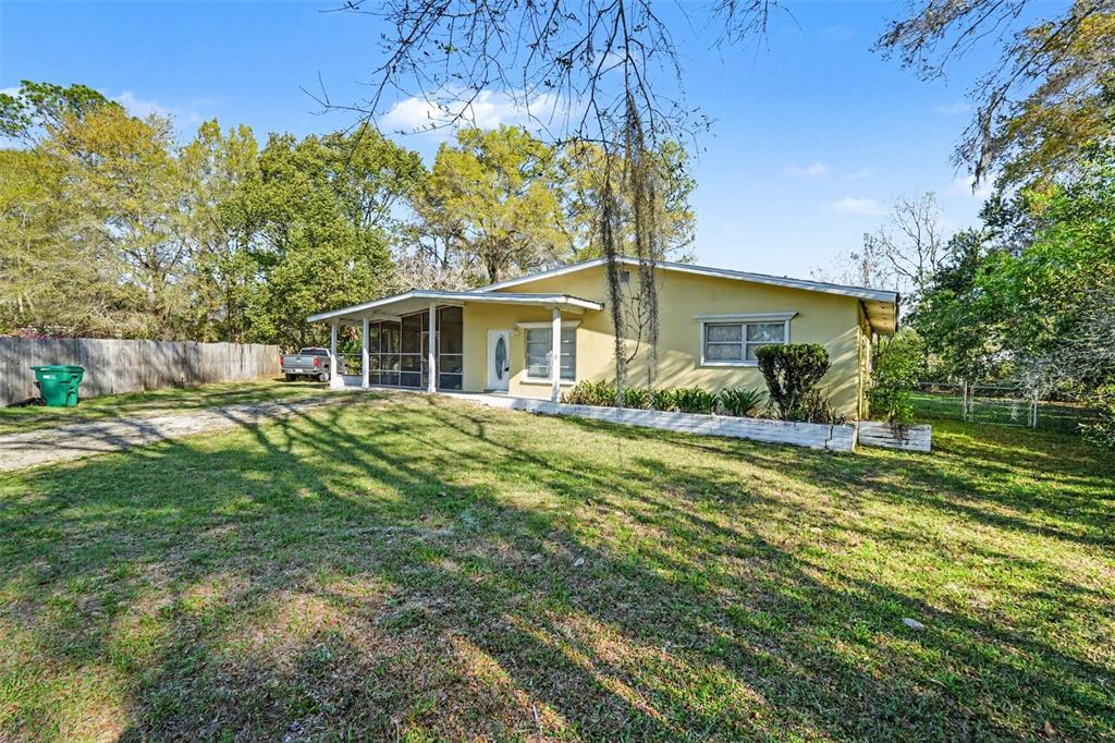 A yellow single-story house with a screened-in porch sits on a grassy lot with trees — 9101 S SUNSET POINT, FLORAL CITY, FL