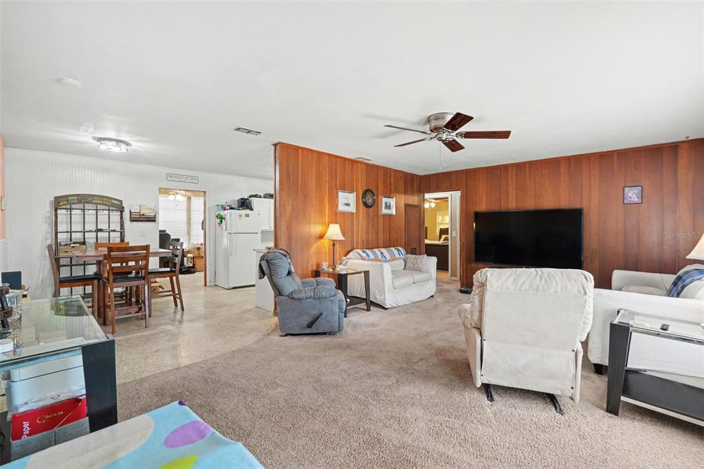 A living room with wood-paneled walls and carpeted floors opens into a dining area — 9101 S SUNSET POINT, FLORAL CITY, FL