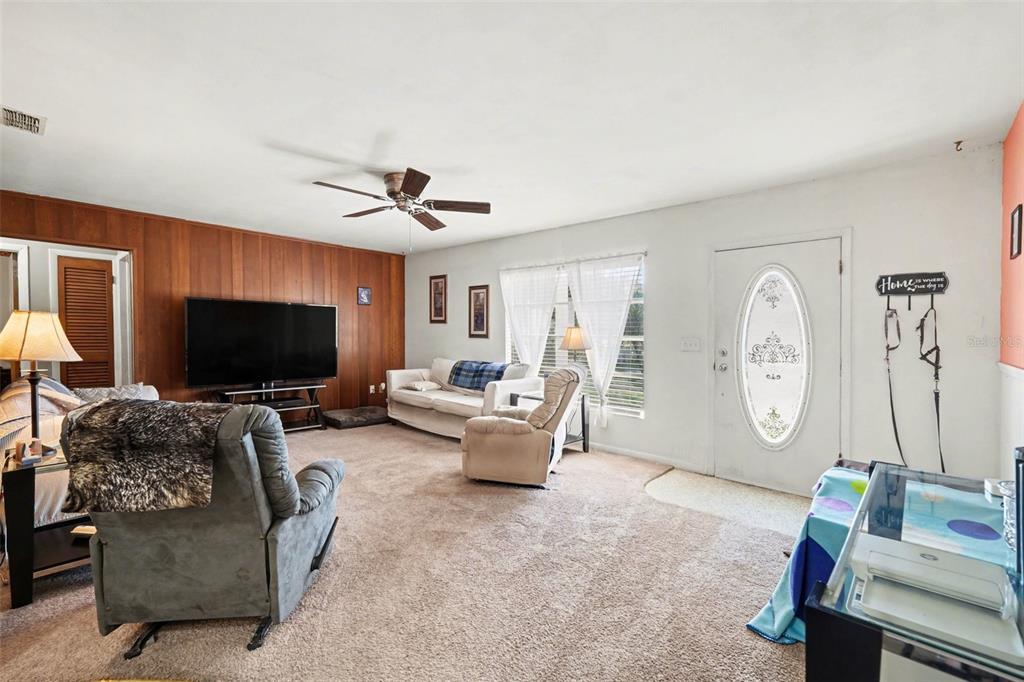 A living room features wood-paneled walls, beige carpeting, a ceiling fan, and an entry door — 9101 S SUNSET POINT, FLORAL CITY, FL