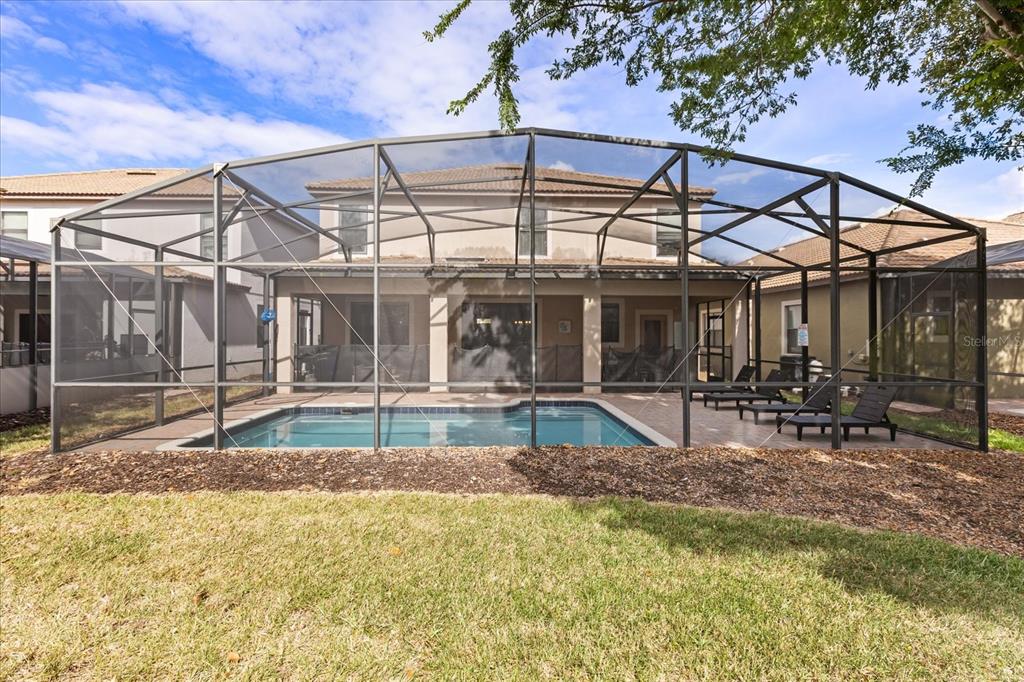 A swimming pool with a screened-in enclosure sits behind a two-story house — 1454 MYRTLEWOOD STREET, DAVENPORT, FL