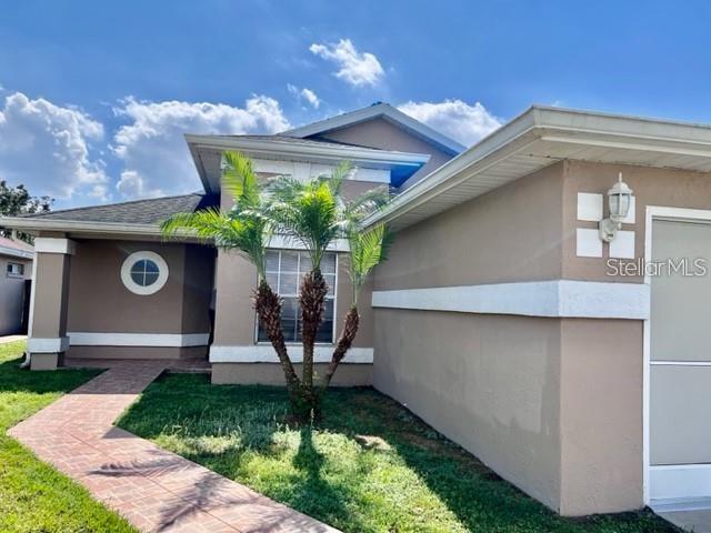 A tan house exterior features a brick walkway, a small palm tree, and a circular window — 3072 STILLWATER DRIVE, KISSIMMEE, FL
