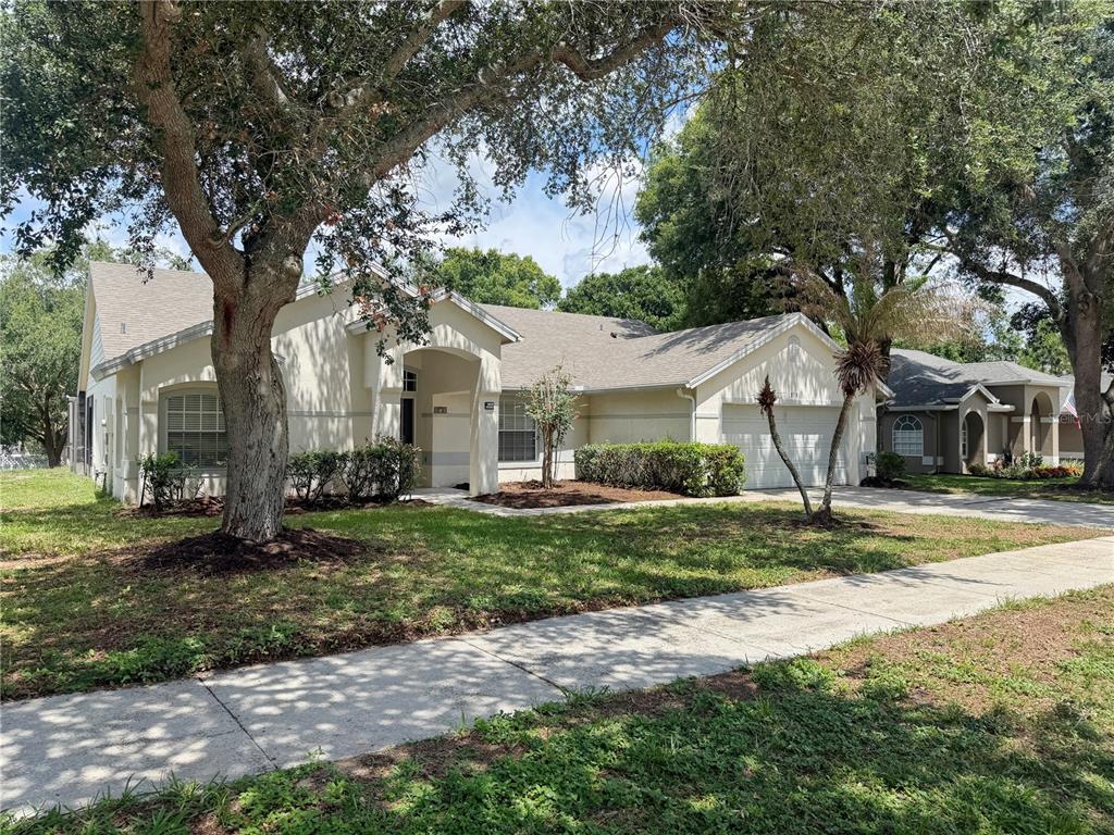 A single-story house with a beige exterior, a two-car garage, and large shade trees — 878 HIGH POINTE CIRCLE, MINNEOLA, FL