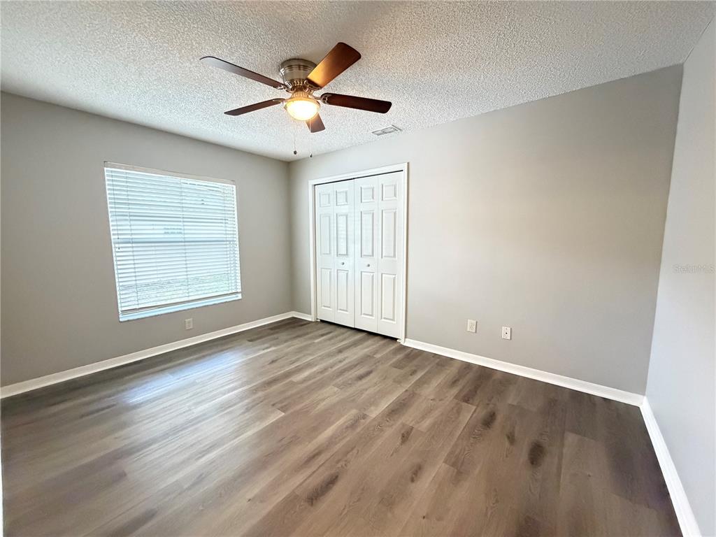 An empty bedroom features light gray walls, wood-look flooring, a ceiling fan, and white closet doors — 878 HIGH POINTE CIRCLE, MINNEOLA, FL