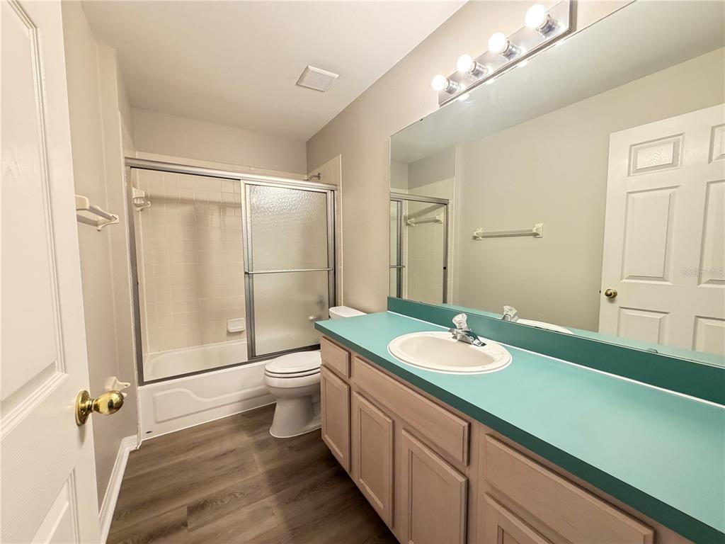 A bathroom features a teal vanity countertop, a shower-tub combination, and wood-look flooring — 878 HIGH POINTE CIRCLE, MINNEOLA, FL