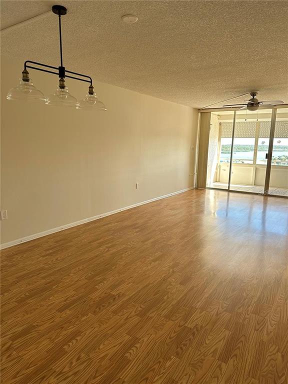 An empty room features wood-look flooring, a modern three-light chandelier, and a sliding glass door — 17920 GULF BOULEVARD UNIT 1408, REDINGTON SHORES, FL