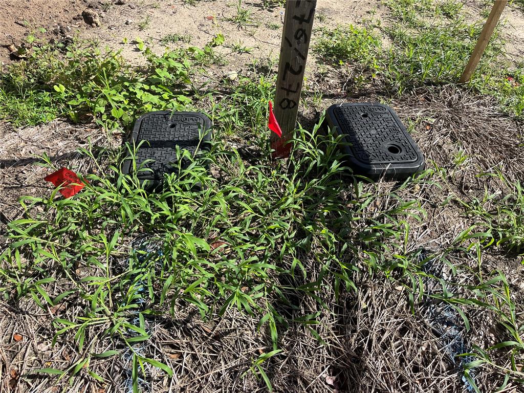 Two black utility boxes sit in a grassy area next to a wooden survey stake — 276 NW 12TH AVE, GAINESVILLE, FL