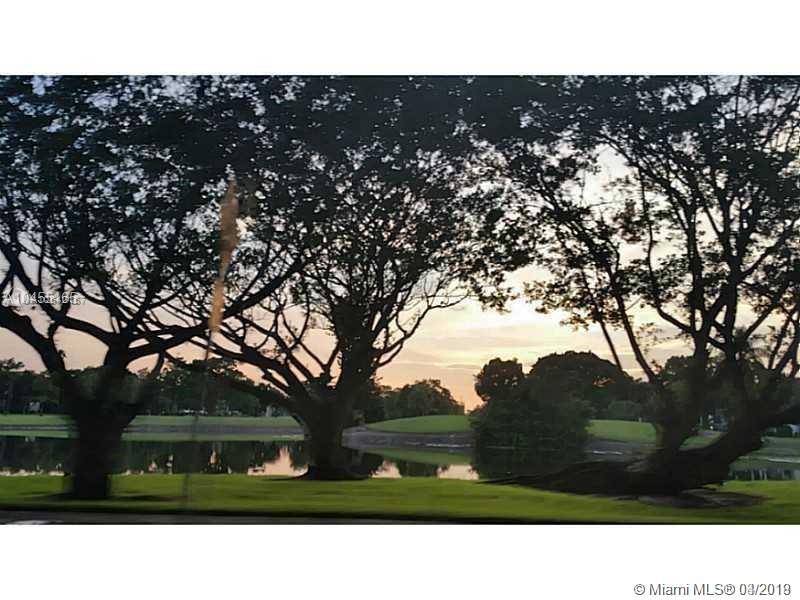 A view of a pond and green lawn framed by large trees at sunset — 4164 Inverrary Dr # 813, Lauderhill FL 33319, LAUDERHILL, FL