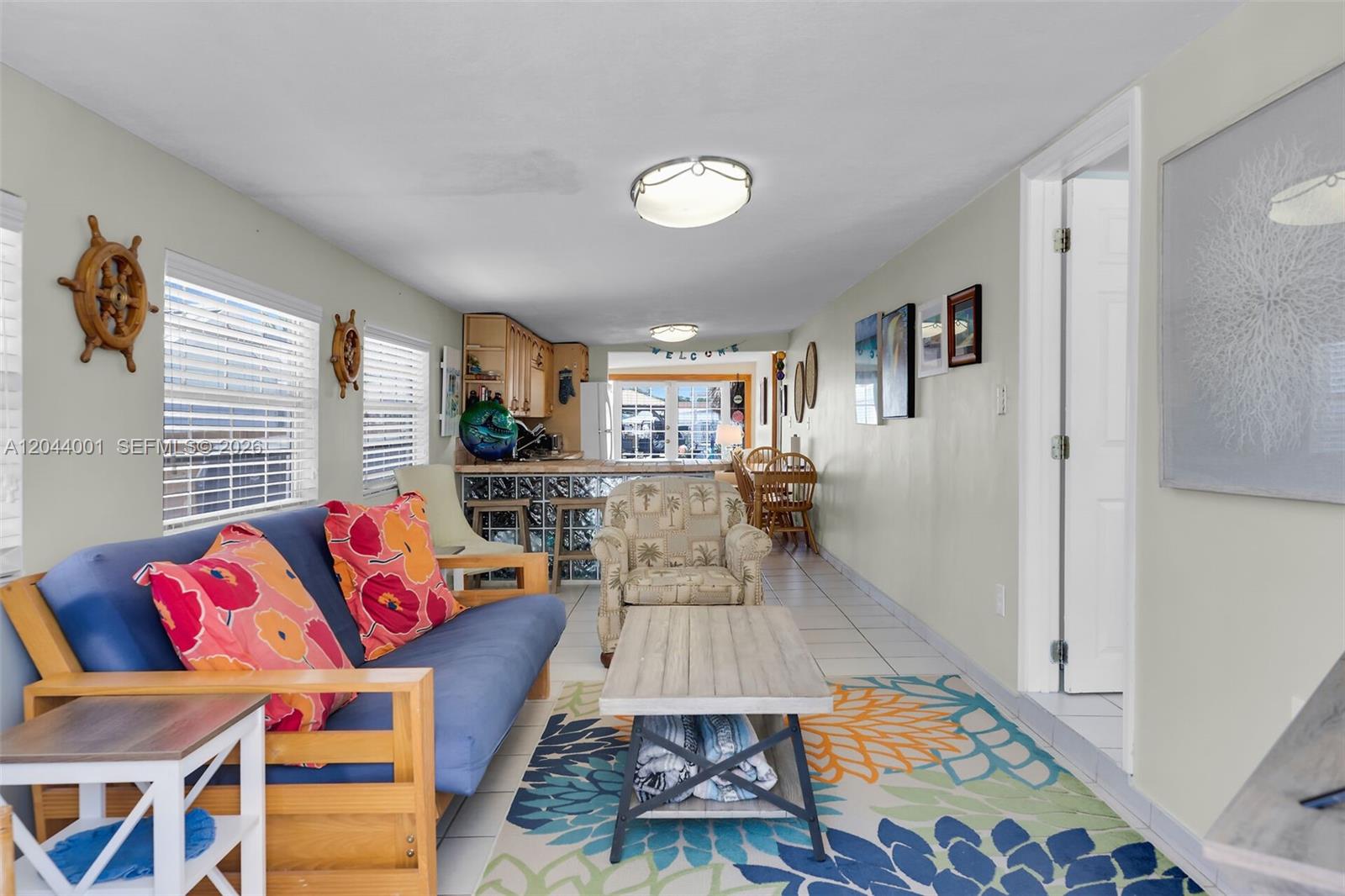 A living room with a blue futon, patterned rug, and an open kitchen beyond — 224 W 1st Ct, Key Largo FL 33037, KEY LARGO, FL