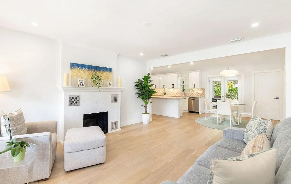 A bright living room with a white fireplace, light wood floors, and an open kitchen — 803 Kanuga Drive, West Palm Beach FL 33401, WEST PALM BEACH, FL