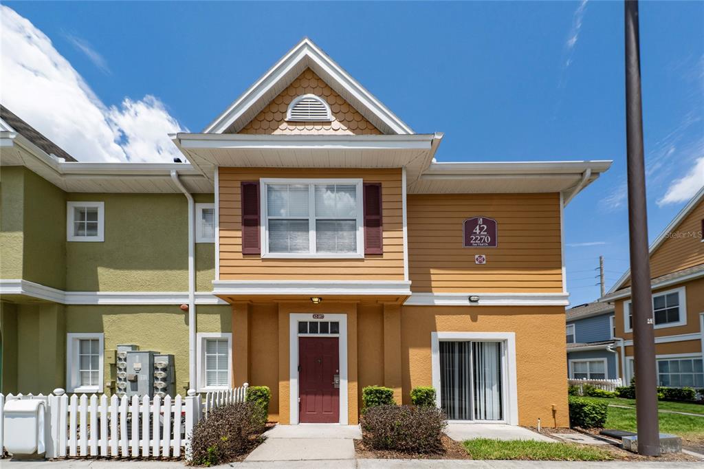 A two-story townhouse with yellow siding, a red front door, and a white picket fence — 2270 SAN VITAL DRIVE UNIT 107, KISSIMMEE, FL