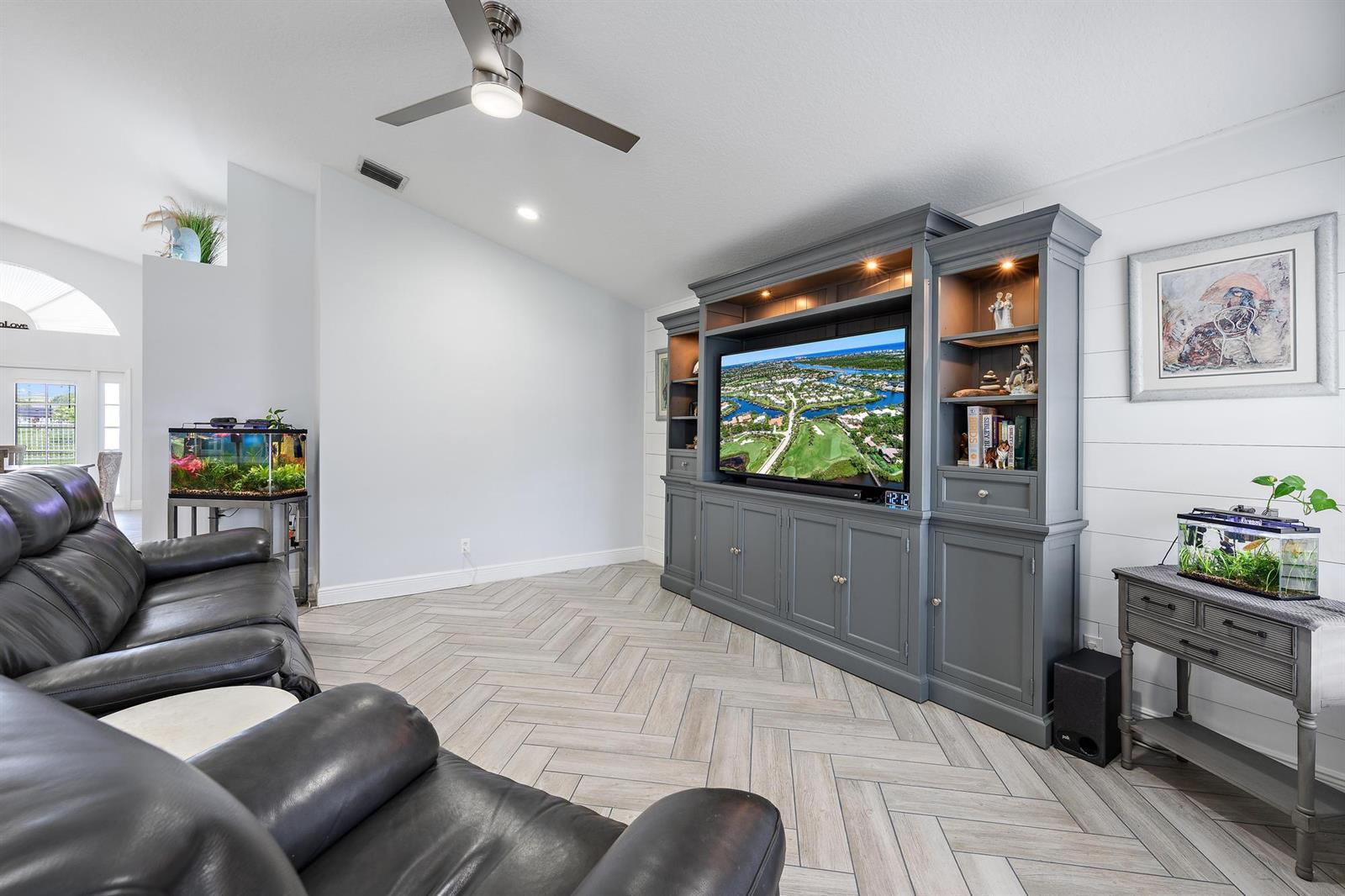 A living room features a large gray entertainment center, leather recliners, and herringbone tile flooring — 1875 Oak Berry Circle, Wellington FL 33414, WELLINGTON, FL