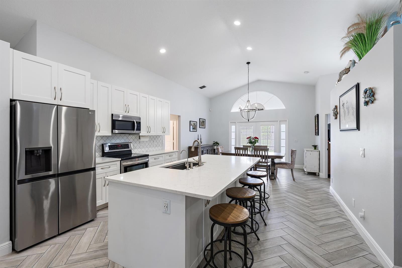 A modern kitchen features white cabinetry, a large quartz island, and herringbone-patterned wood-look flooring — 1875 Oak Berry Circle, Wellington FL 33414, WELLINGTON, FL