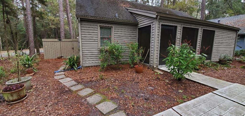 A single-story house with tan siding sits behind a low wooden fence in a wooded area — 5201 SW 86 TERRACE, GAINESVILLE, FL