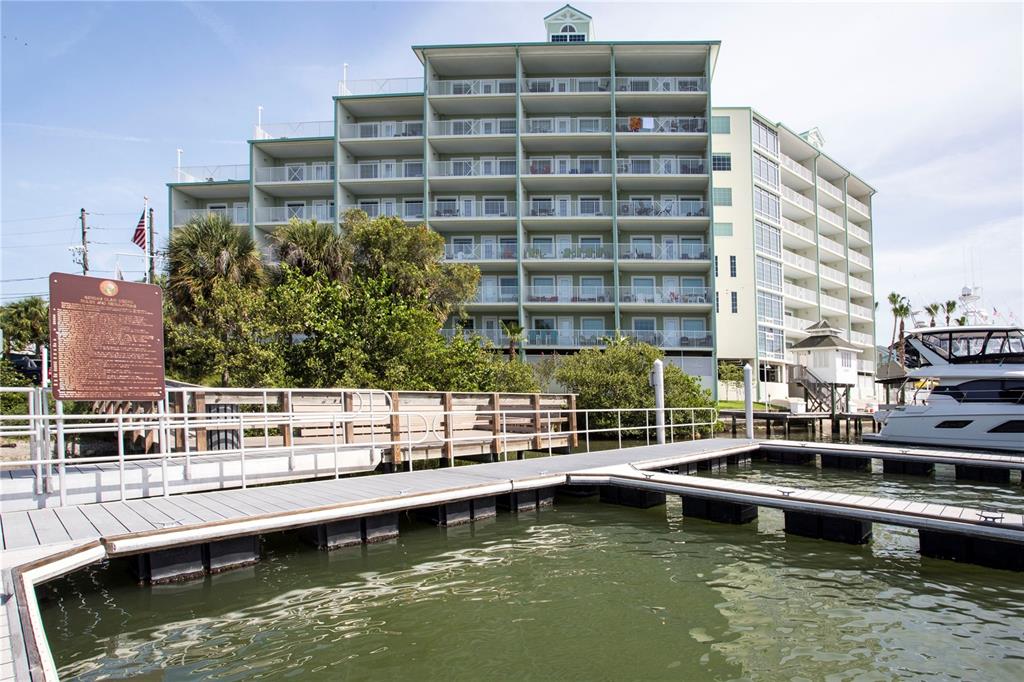 A multi-story waterfront condominium building sits behind a wooden dock and boat slip — 399 2ND STREET UNIT 417, INDIAN ROCKS BEACH, FL