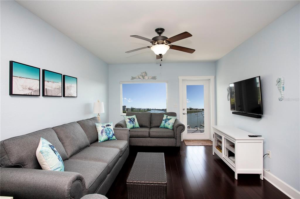 A living room features gray sofas, a coffee table, a television, and a water view — 399 2ND STREET UNIT 417, INDIAN ROCKS BEACH, FL