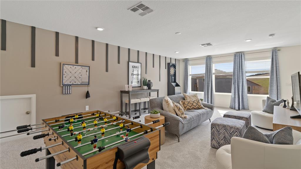 A game room features a foosball table, a gray sofa, and wall-mounted decorative wood slats — 171 GLENFIELD DRIVE, DAVENPORT, FL