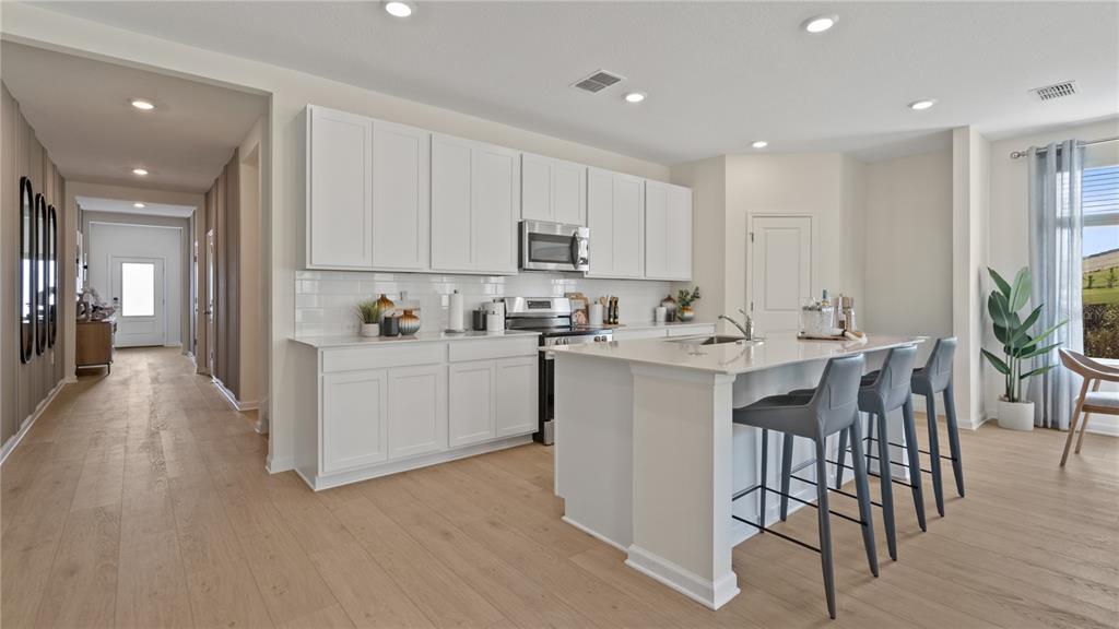 A modern kitchen features white cabinets, a central island with bar seating, and light flooring — 171 GLENFIELD DRIVE, DAVENPORT, FL