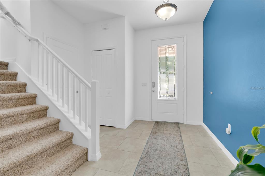 An entryway features a carpeted staircase, tile flooring, a white front door, and blue walls — 8819 TATARA STREET, ORLANDO, FL
