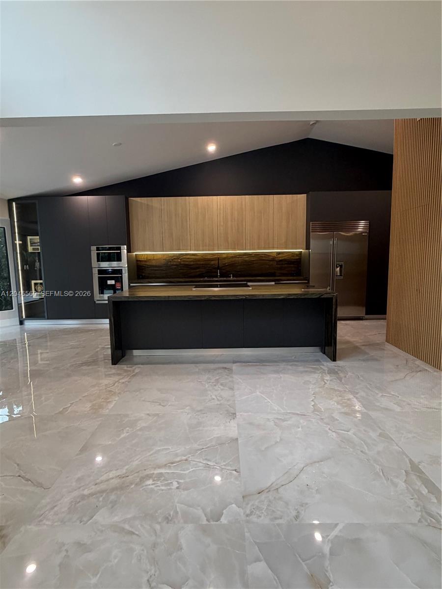 A modern kitchen features dark cabinetry, wood-toned upper cabinets, a large island, and marble flooring — 4499 NW 93rd Doral Ct, Doral FL 33178, DORAL, FL