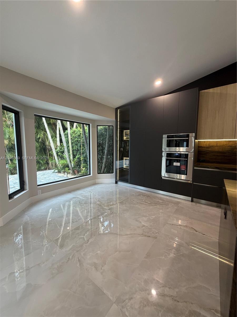 A modern kitchen features dark cabinetry, built-in stainless steel ovens, and large polished marble floors — 4499 NW 93rd Doral Ct, Doral FL 33178, DORAL, FL