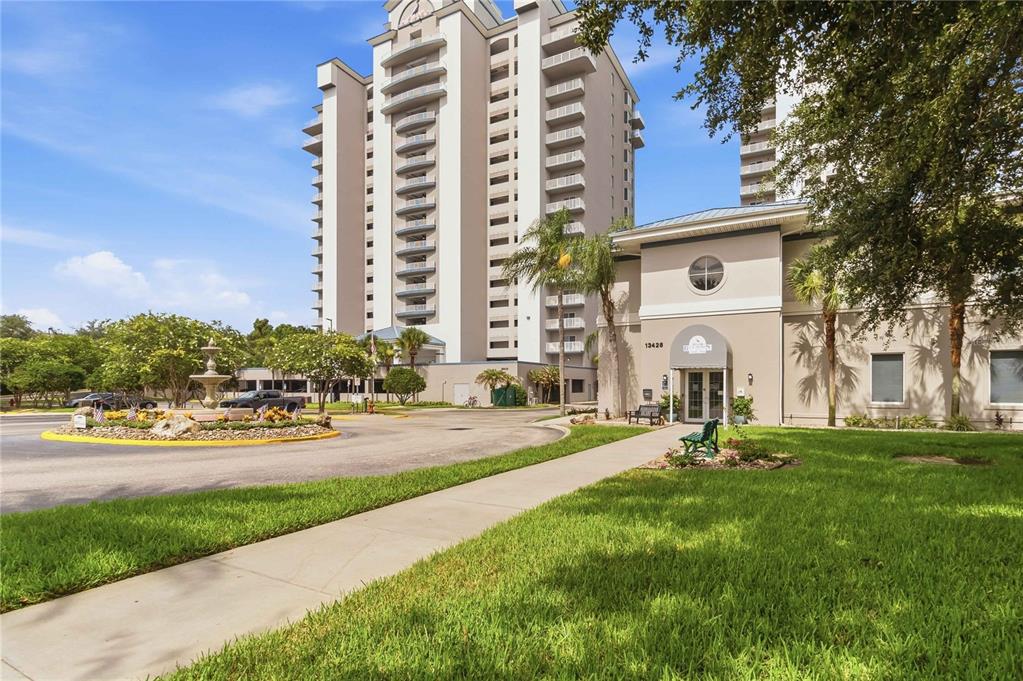 A tall apartment building stands behind a circular driveway with a central fountain — 13427 BLUE HERON BEACH DRIVE UNIT 104, ORLANDO, FL