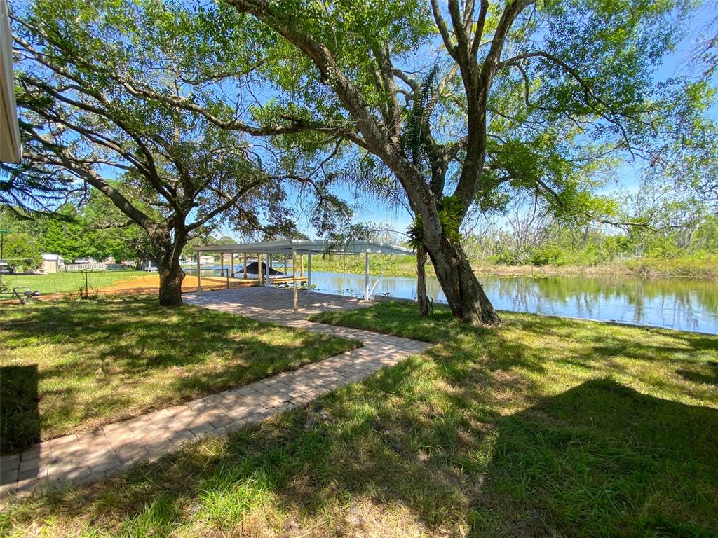 A paved walkway leads through a grassy yard toward a covered patio by a lake — 28046 LOIS DRIVE, TAVARES, FL