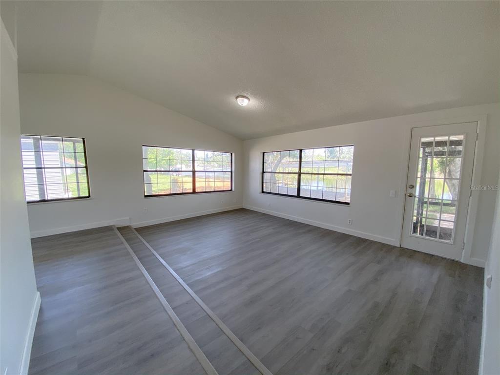 A living room with light gray wood-look flooring, white walls, and multiple windows overlooking water — 28046 LOIS DRIVE, TAVARES, FL