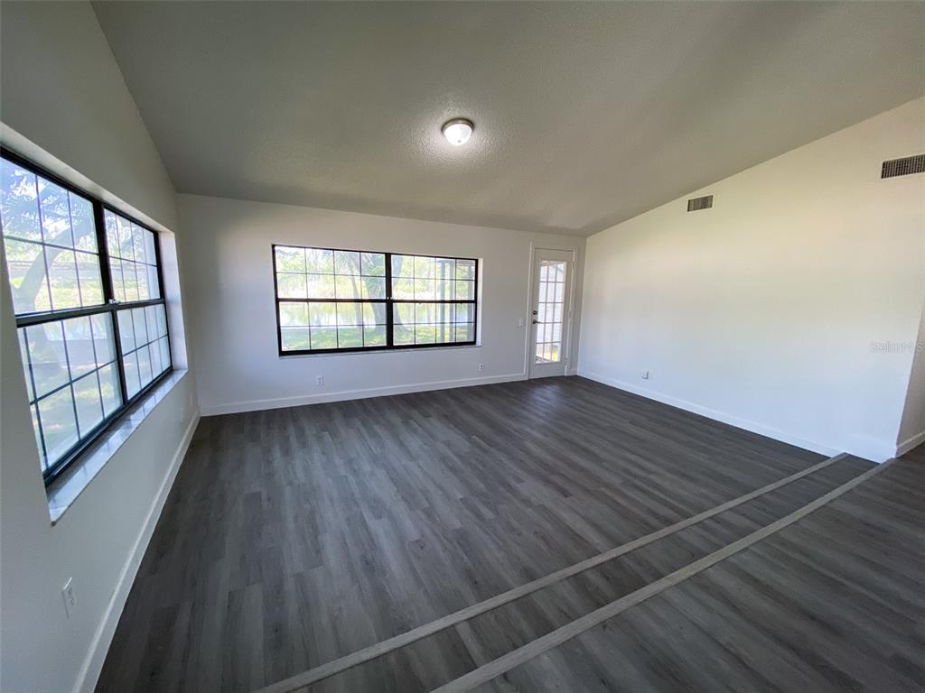 An empty room features gray wood-look flooring, white walls, large windows, and a glass door — 28046 LOIS DRIVE, TAVARES, FL