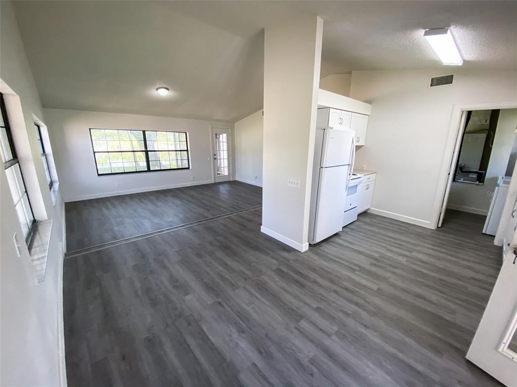 A bright living area with gray wood-look flooring flows into a kitchen with white appliances — 28046 LOIS DRIVE, TAVARES, FL