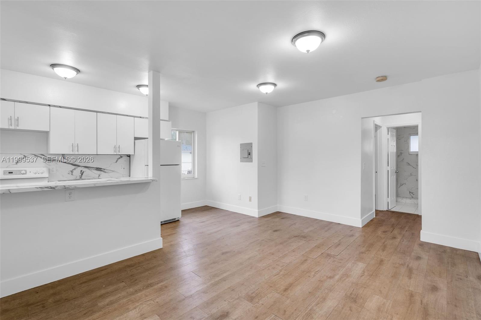 A kitchen with white cabinets and a living area with wood-look flooring — 5549 NE Miami Ct # 1, Miami FL 33137, MIAMI, FL