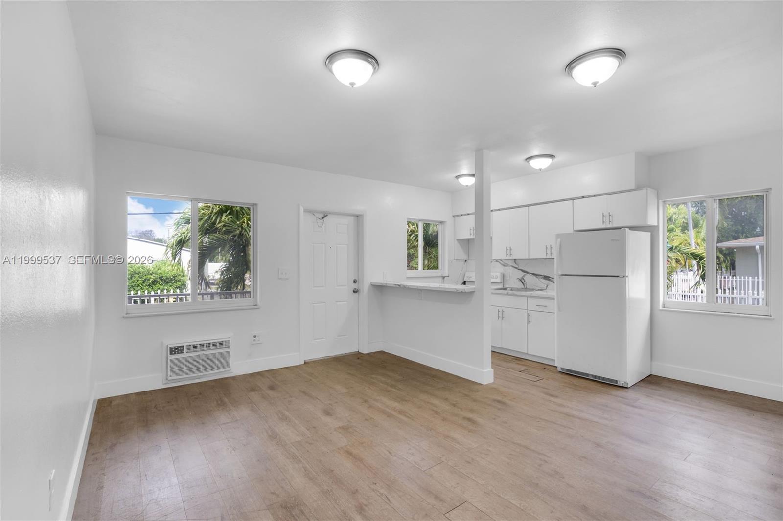 This open-concept living area features white walls, light wood flooring, and a small kitchen — 5549 NE Miami Ct # 1, Miami FL 33137, MIAMI, FL